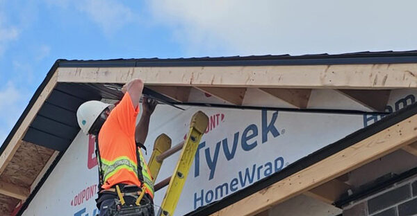 soffit-replacement-chatham-kent-ontario Image of an Aurora Exteriors Inc employee affixing black vented aluminum soffit material to a new construction home.