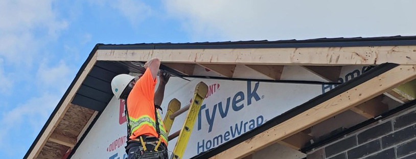 Image of an Aurora Exteriors Inc employee affixing black vented aluminum soffit material to a new construction home.