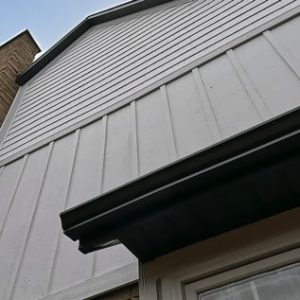 White engineered board and batten siding and contrasting black soffit, fascia and eaves troughing.