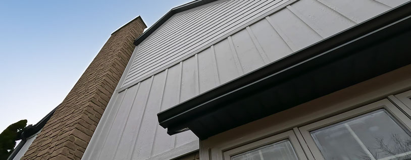 White engineered board and batten siding and contrasting black soffit, fascia and eaves troughing.