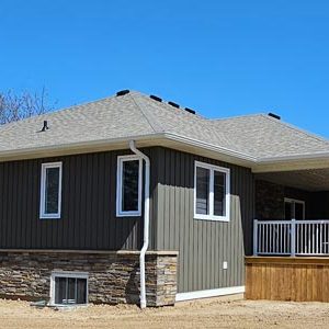 Image of the back right corner of a custom built home finished by Aurora Exteriors Inc featuring Vertical vinyl in a castlemore colour and versetta stone in sterling