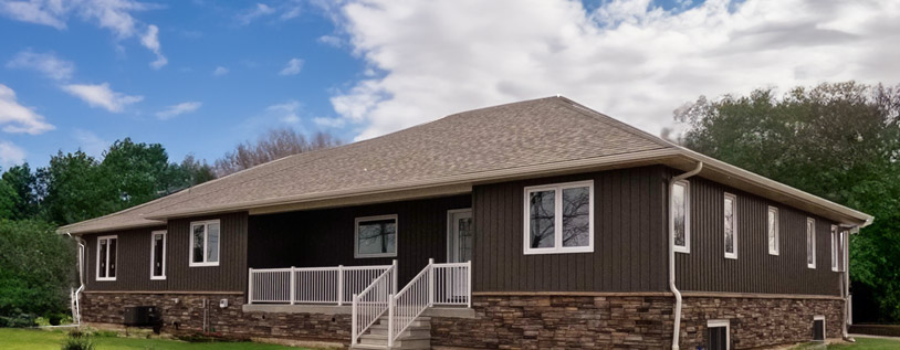 Image of A Custom Built Home Exterior Finished by Aurora Exteriors Inc to include Faux Stone, Vertical Vinyl, Aluminum Railings, Aluminum Post Wraps, a back deck and white aluminum soffit, fascia and eaves.