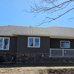 The front view of a custom built home finished by Exterior Finishing company Aurora Exteriors in a stunning vertical vinyl in a castlemore colour, versetta stone skirting in sterling and white aluminum railings on the front porch.