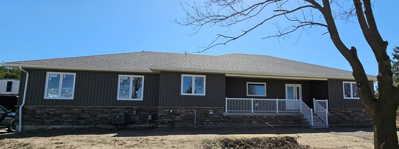 The front view of a custom built home finished by Exterior Finishing company Aurora Exteriors in a stunning vertical vinyl in a castlemore colour, versetta stone skirting in sterling and white aluminum railings on the front porch.