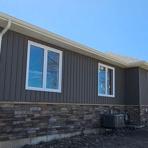 New Construction Home Finished by Aurora Exteriors Inc featuring sterling Versetta Stone Siding, Castlemore Vertical Vinyl siding, and Wolfe White Aluminum Trims and Downspouts.