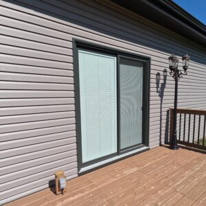 Stonecrest grey vinyl siding cladding the exterior wall of a Shrewsbury Ontario home with newly upgraded dark rustic granite sliding patio door leading to the homes back deck.